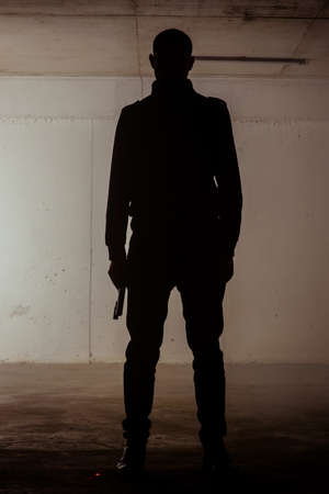 Silhouette of a man standing still with a revolver in his handsの写真素材