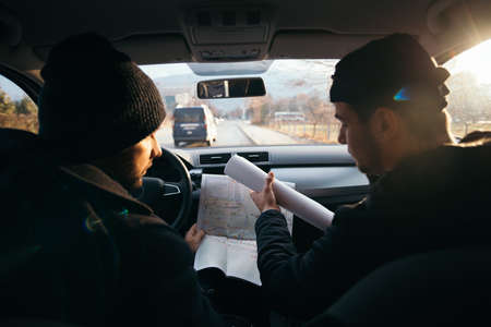 Two violent robbers sitting in a car looking at a blueprint of the building they want to rob while proudly showing off their guns.の写真素材