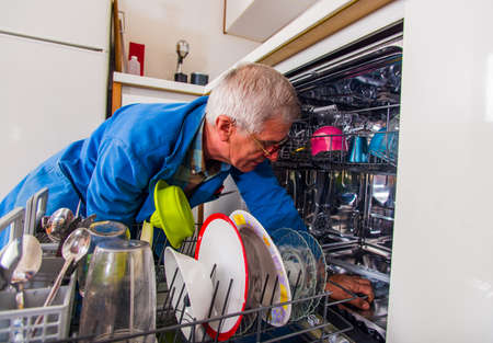Handyman opening the dishwasher machine in white kitchenの写真素材