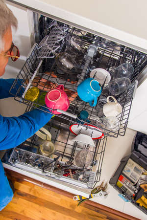 Handyman opening the dishwasher machine in white kitchenの写真素材