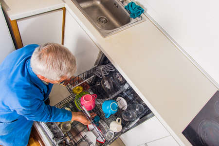 Senior handyman opening dish washer machine in his houseの写真素材
