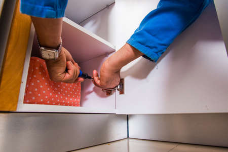 Repairman is holding the screwdriver and fixing the cupboard in the kitchen