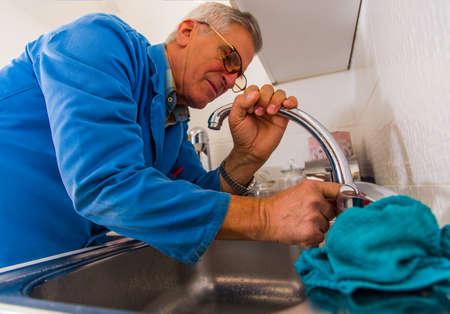 Serious old age repairman is fixing the kitchen tap