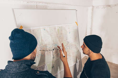 Terorists are standing near the map and looking on the robbery plan