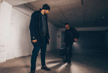 Criminals are standing in a dark garage and showing a bag full of stolen moneyの写真素材