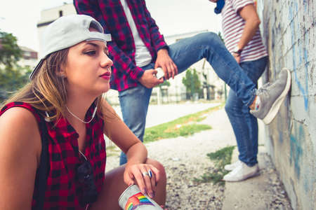 A girl is with her two friends outdoors, writing letteres on old wallの写真素材