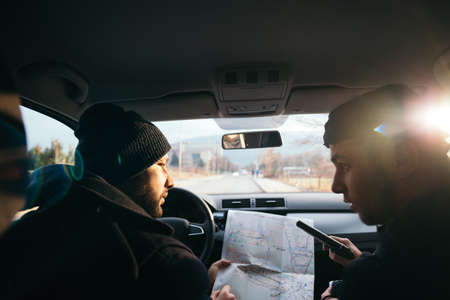 Criminals sitting at sunset in a car, looking at the city map and planning their next move.