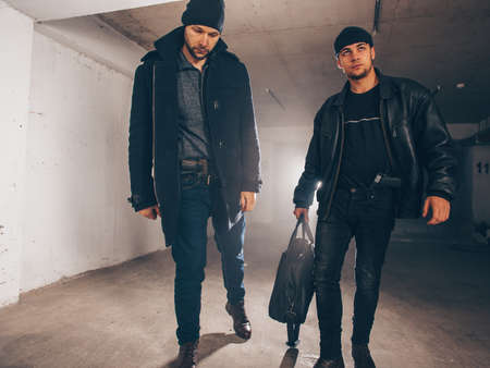 Burglars are standing in a dark hallway, holding a bag full of money