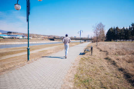 Athletic young man running on a track next to a river while wearing headphones.
