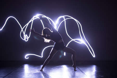 Modern Dance performer dancing with a neon blue light while making gracious moves and spectacular body art expressions.の写真素材