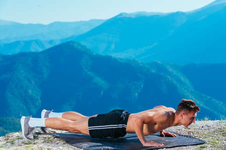 Handsome athlete ( sportsman ) doing push ups on top of a mountant whit an amazing view on the...