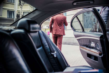Businessman in suit standing outside from his luxury car and talking on mobileの写真素材