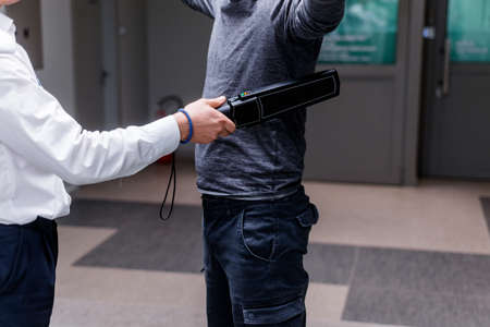 Guard with a metal detector checking a man for weapons and metal objects before entering in treasury departmentの写真素材