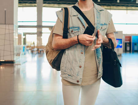 Casually dressed man with backpack and tickets is looking at timetable while standing in airport terminal hallの写真素材