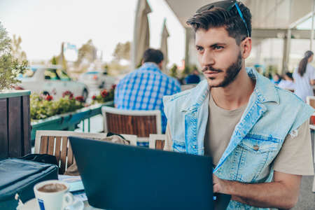 Young businessman reading emails on laptop in modern coffee shop at airportの写真素材