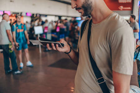 Young handsome man in 20s waiting for flight, standing in modern airport terminal