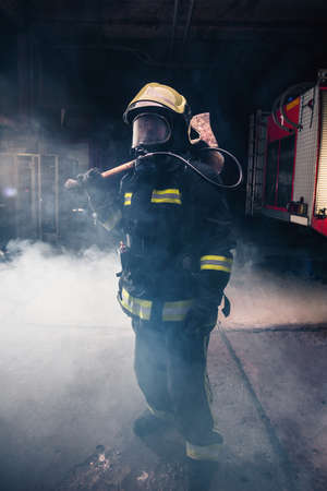 Portrait of a female firefighter while holding an axe and wearing an oxygen mask indoors surrounded by smoke.の写真素材