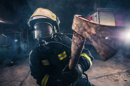 Portrait of a female firefighter while holding an axe and wearing an oxygen mask indoors surrounded by smoke.の写真素材