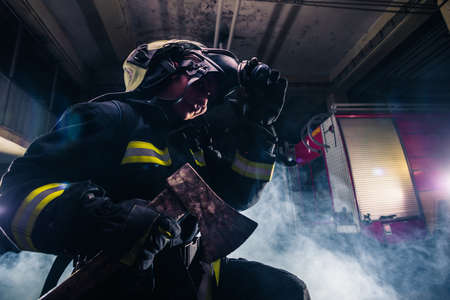Portrait of a female firefighter while holding an axe and wearing an oxygen mask indoors surrounded by smoke.の写真素材