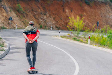 Tall athlete riding his longboard fast and steady downhill while wearing red t-shirt and black jeans.の写真素材