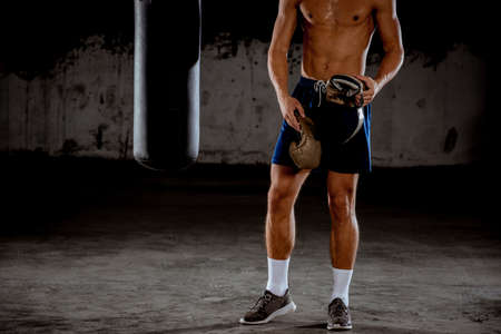 Determined young Muay Thai fighter in boxing gloves training thai boxing with punching bagの写真素材