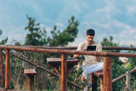 Young smiling hipster man relaxing and having a break at the park and using a tabletの写真素材