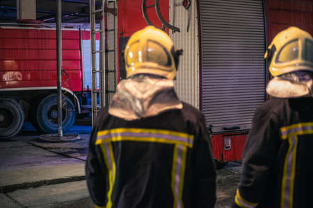 Two young men wearing helmets posing from the back inside the fire station.