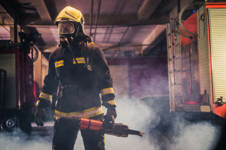 Portrait of young fireman standing and holding a chainsaw in the middle of the chainsaw's smokeの写真素材