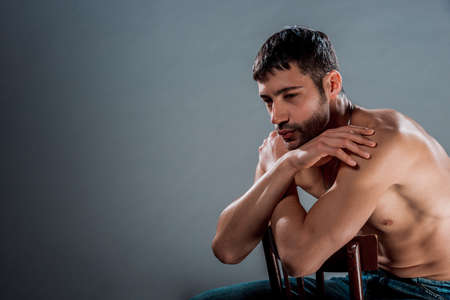 Torso shot of a sexy shirtless man sitting on a wooden chair