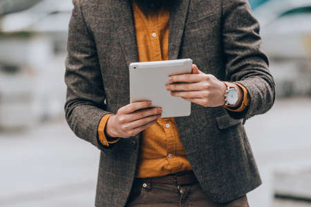 Young caucasian guy clothed in a fashionable costume holding a tablet computer