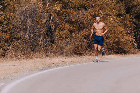 Full length of fit young male runner exercising on mountain road. Athlete running down the hill on mountain roadの写真素材