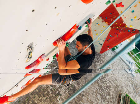Young man climbs up an outdoors rock wall