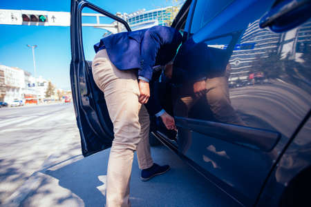 Happy entrepreneur opening his car door and inspecting the interior of his car while being parked...