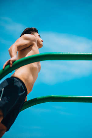 Handsome young man doing street workout on the beach on chin up bar