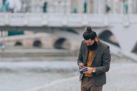 Fashionable male dressed in expensive outfit working on his phone at the city promenade