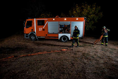 Fire service team in uniform with protective helmets extinguishing a fire in the area