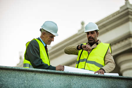 Senior and handsome construction worker is checking the time