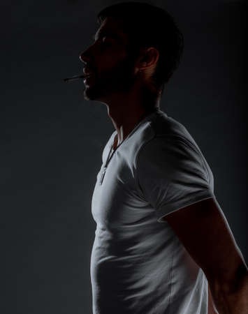 Cool trendy guy wearing stylish white t-shirt and smoking a cigaretteの写真素材