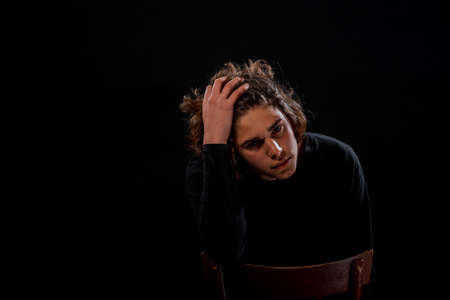 Portrait of an attractive stylish man sitting on a chair posing against dark backgroundの写真素材