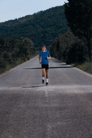 Male athlete running on an empty road in the woods while trying to get to the red finish line.の写真素材