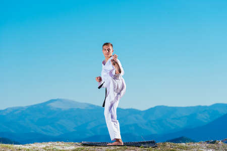 Blond karate athlete does kata on top of a mountain while performing a line up of kicks, punches and blocks on top of a mountain on a sunny day.の写真素材