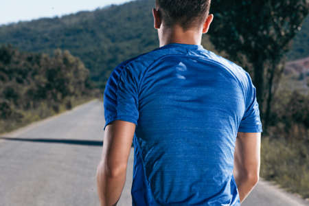 Close up portrait of a blonde, sweaty male runner (athlete). Running on an empty road in the woods.の写真素材