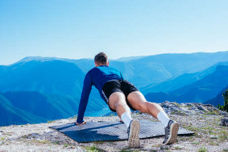 Strong handsome blonde athlete doing push ups on top of and mountain while enjoying the amazing view...