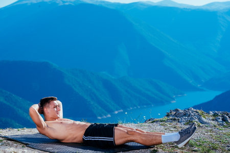 A strong fit male athlete has an abs workout on top of a mountain.
