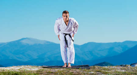 Karate athlete bows down while wearing his kimono on top of a mountain.