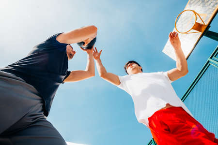 Two caucasian basketball player fighting for ball possession at the basketball court on a sunny day.の写真素材