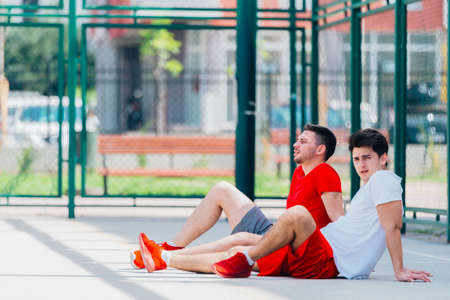 Two friends after a long hard basketball game have some rest on the basketball court sitting next to...