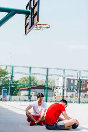 Two strong caucasian athletes resting on the ground at the basketball court while having a...