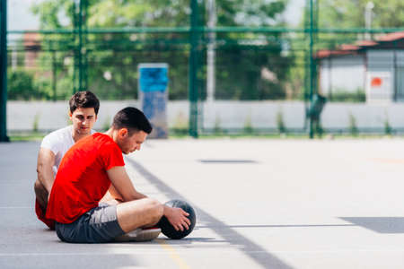 Two strong caucasian athletes resting on the ground at the basketball court while having a conversation.の写真素材