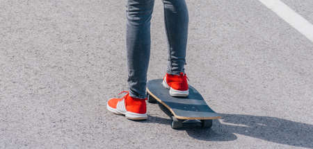 Male caucasian longboarder riding downhill on an empty road doing a speed tuck and grabbing the board while driving the longboard fast. Wearing a red t-shirt green hat and black jeans.の写真素材